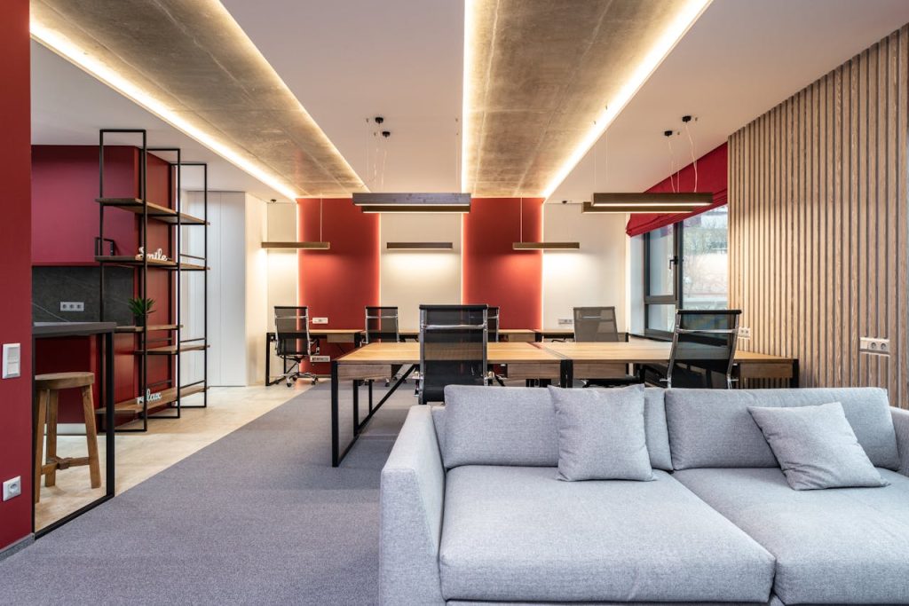 lounge-zone-in-office-with-couch-near-tables-with-chairs-6899397 Spacious modern office featuring red accent walls, stylish furniture, and ample natural light.