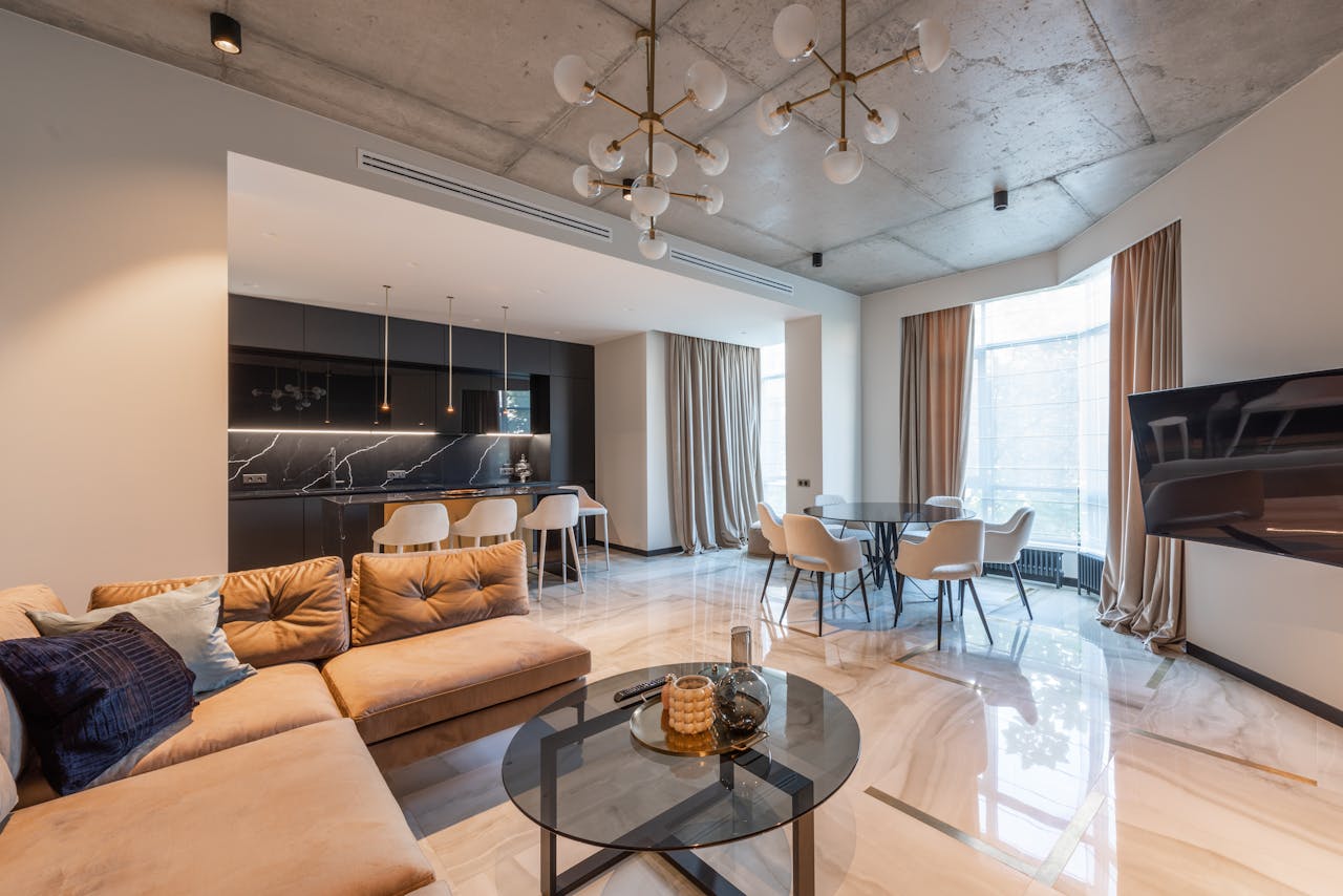 our-journey-02 Interior of contemporary flat with sofa with pillows near kitchen with counter and round table with chairs near TV under chandelier near windows with curtains